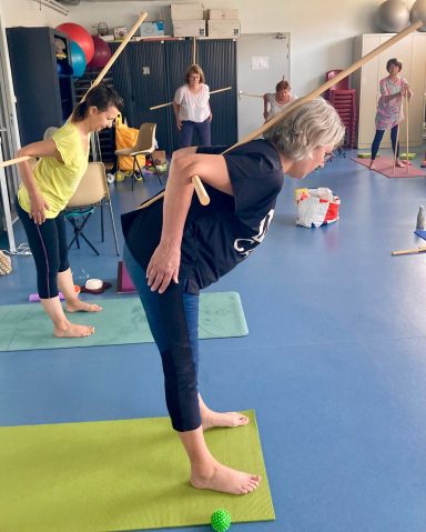 Posture de la demi-pince en yoga avec 2 bâtons pour corriger l'alignement du dos, pratiqué dans la salle de yoga de Eysines