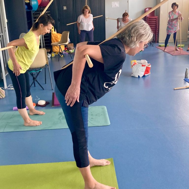 Le bâton comme accessoire aide à ressentir le bon alignement et à corriger les compensations lombaires, en gardant la colonne neutre.